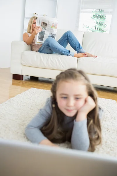 Chica trabajando con el ordenador portátil con su madre leyendo el periódico — Foto de Stock