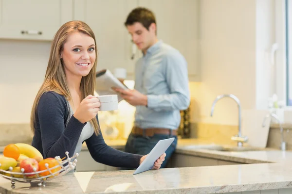 Woman drinking hot beverage using tablet pc in kitchen — Stock Photo, Image