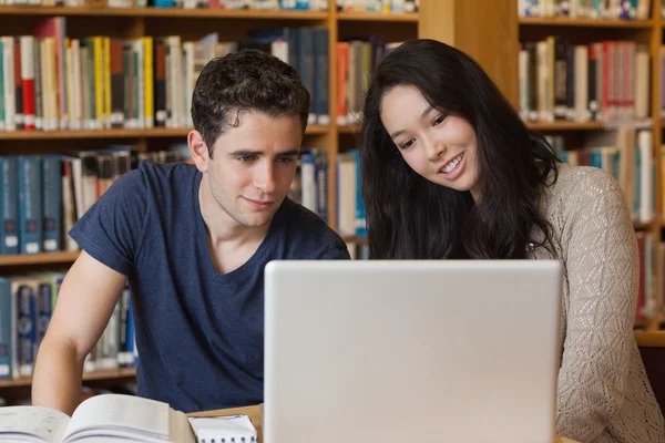 Dois alunos aprendendo em uma biblioteca com um laptop — Fotografia de Stock