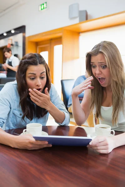 Women looking surprised while holding a tablet — Stock Photo, Image