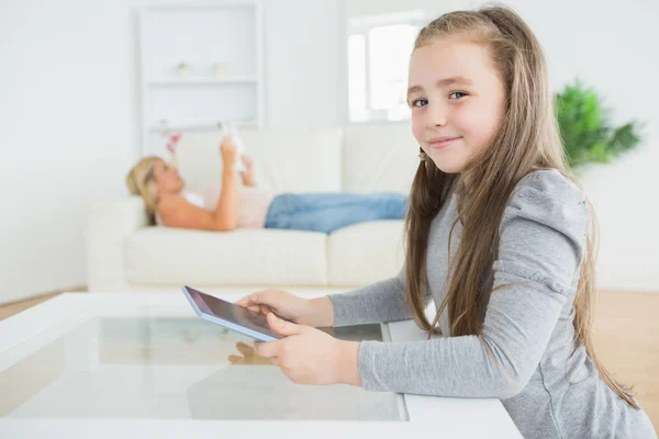 Niña usando tableta mientras madre está leyendo periódico —  Fotos de Stock