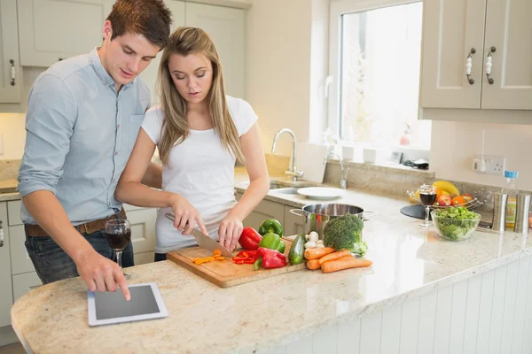 Mulher cortando legumes com o homem usando tablet computador — Fotografia de Stock