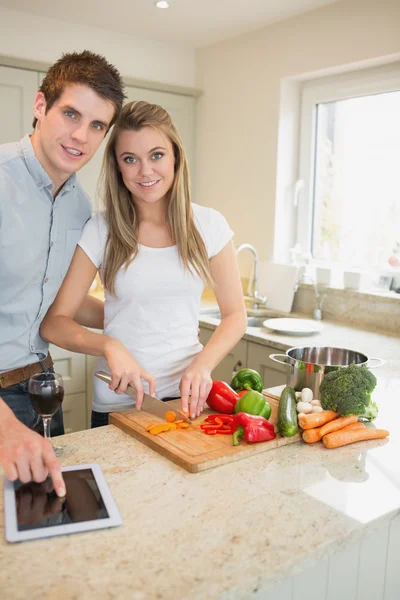 Femme hachant des poivrons avec l'homme tapant sur le comprimé pc — Photo