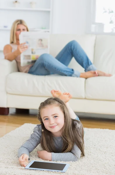 Souriant petite fille à l'aide d'une tablette tandis que sa mère lit le journal — Photo