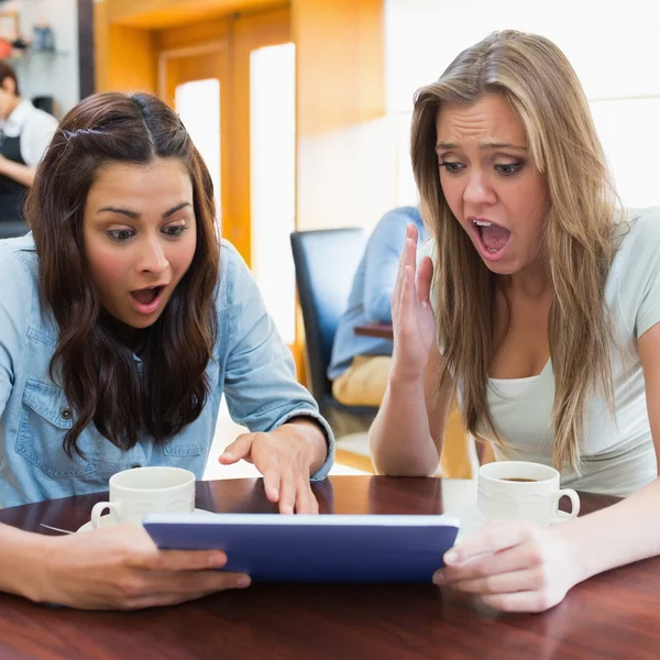 Women looking shocked at tablet pc in canteen Royalty Free Stock Photos