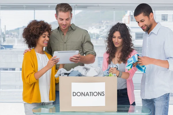 Voluntarios usando tableta y sacando ropa de una caja de donaciones —  Fotos de Stock