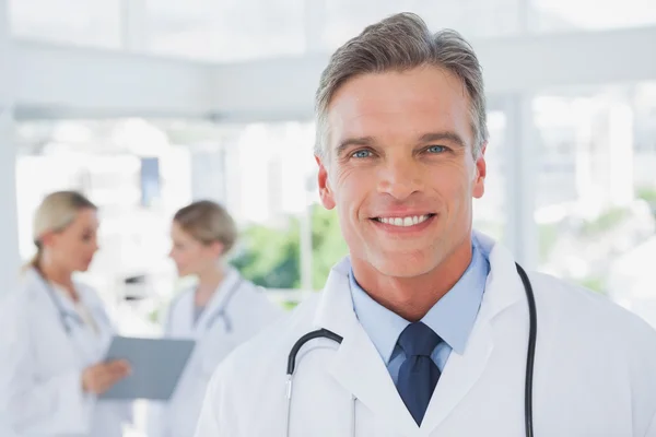 Usmívající se šedými vlasy doktor stojící ve své kanceláři — Stock fotografie