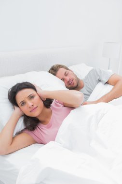 Annoyed woman covering her ears while her husband is snoring clipart