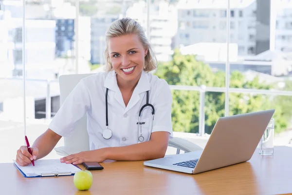 Schöne Krankenschwester schreibt auf einem Notizblock auf ihrem Schreibtisch — Stockfoto