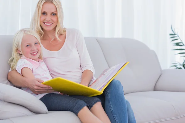 Madre e hija sentadas en un sofá leyendo un libro — Foto de Stock