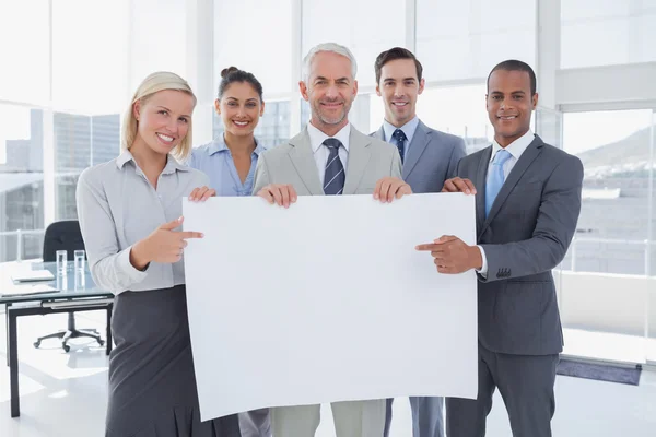 Business team holding large blank poster and pointing to it — Stock Photo, Image