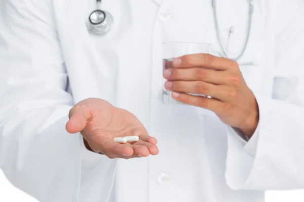 Médico segurando pílulas e vidro de água — Fotografia de Stock