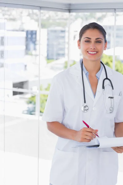 Doctor smiling at camera and holding clipboard and pen — Stock Photo, Image