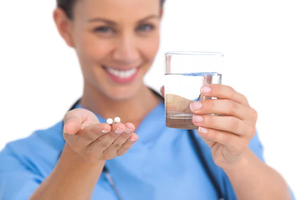 Smiling surgeon holding medicine and glass of water — Stock Photo, Image