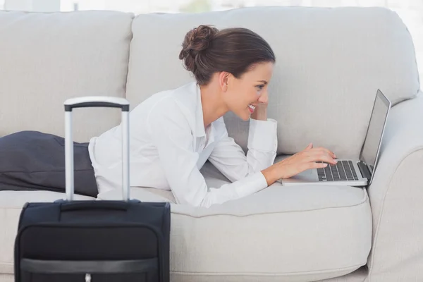 Mujer de negocios acostada en el sofá con el ordenador portátil y la maleta — Foto de Stock