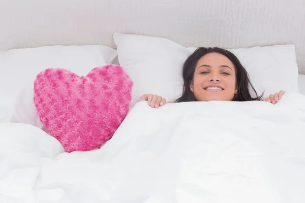 Kabarık kalp yastık yanındaki yatakta yatan kadın — Stok fotoğraf
