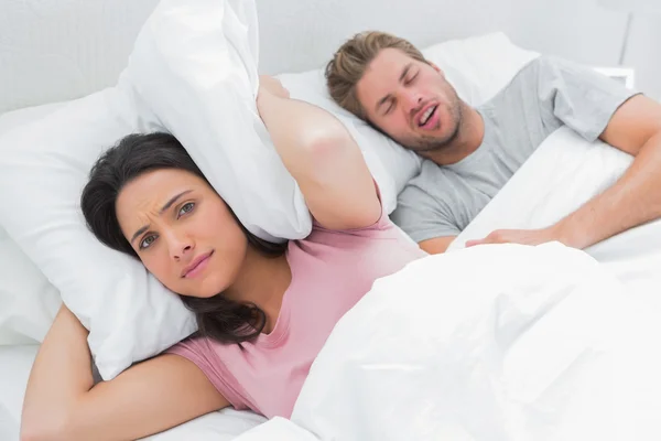 Mujer cubriendo orejas con almohada mientras su marido ronca — Foto de Stock