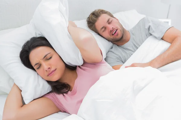 Woman covering her ears with pillow while her husband is snoring — Stock Photo, Image