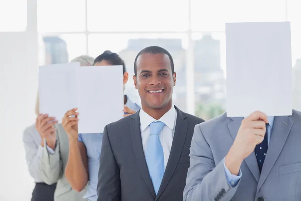 Businessman smiling at camera with colleagues covering faces — Stock Photo, Image