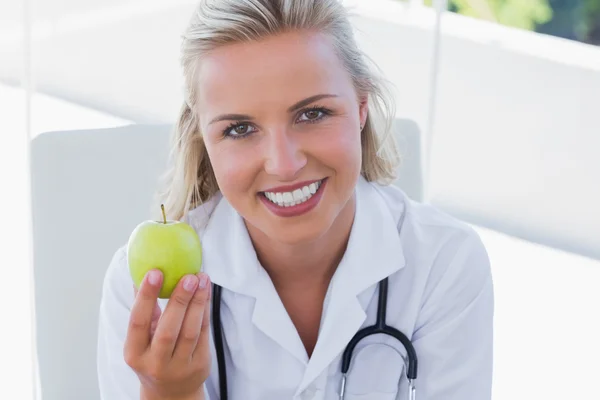 Lachende blonde verpleegster houden een groene appel — Stockfoto