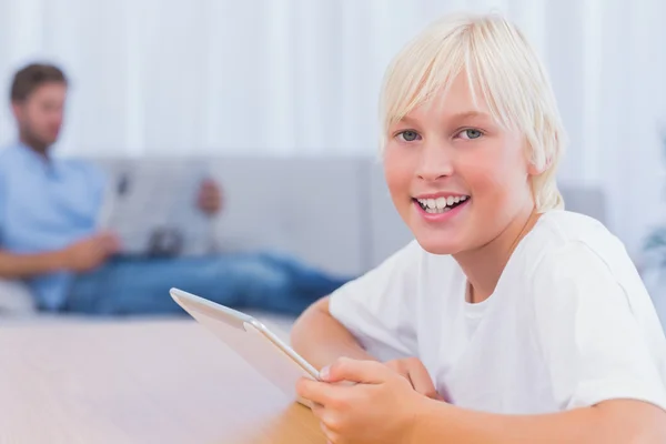 Usměvavý chlapec pomocí tablet, zatímco jeho otec je čtení na couc — Stock fotografie