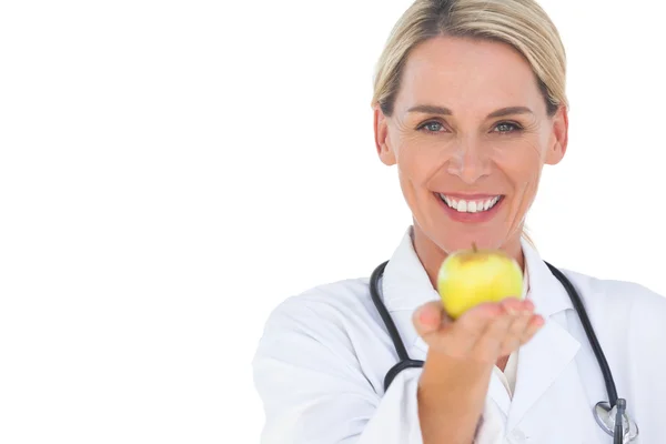 Happy doctor holding out apple and looking at camera — Stock Photo, Image