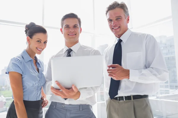 Tres sonrientes negocios sosteniendo un portátil — Foto de Stock