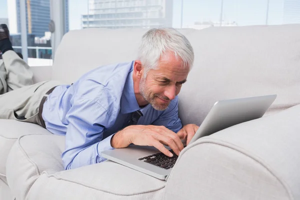 Businessman lying on couch using laptop — Stock Photo, Image