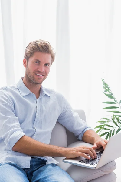 Atrakcyjny mężczyzna siedzi na kanapie i za pomocą jego laptop — Zdjęcie stockowe