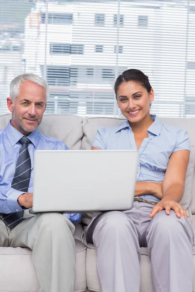 Negócios com laptop sorrindo para a câmera sentada no sofá — Fotografia de Stock