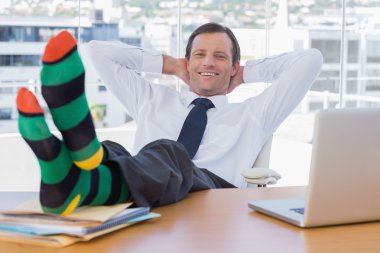 Smiling businessman relaxing with feet on his desk clipart