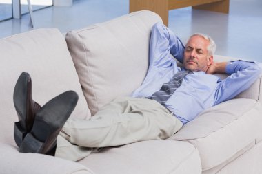 Businessman lying on sofa with his feet up clipart