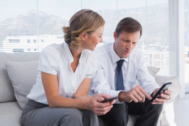 Attractive businessman showing something on his mobile phone to a businesswoman clipart