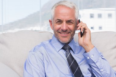 Businessman calling on smartphone and smiling at camera clipart