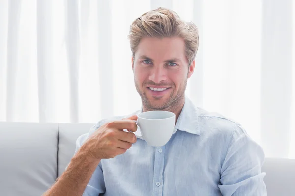 Schöner Mann sitzt auf seinem Sofa und trinkt einen Kaffee — Stockfoto