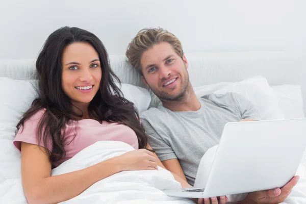 Casal usando um laptop em sua cama — Fotografia de Stock