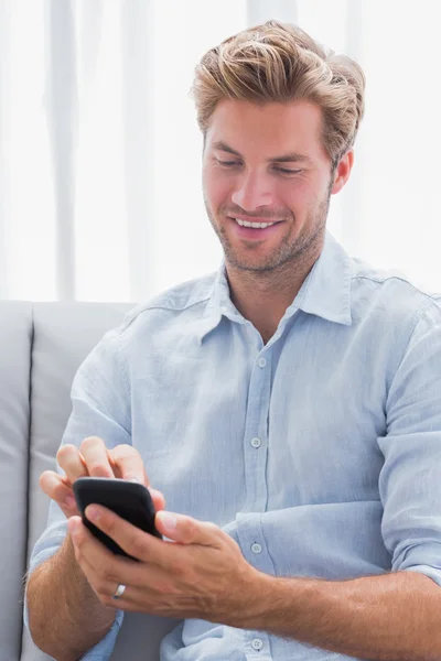 Hombre alegre usando su teléfono inteligente en un sofá — Foto de Stock