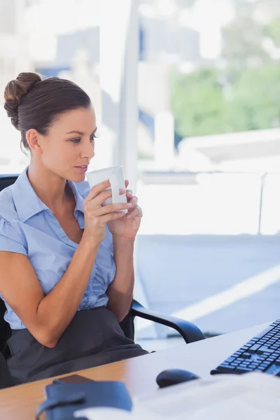 Geschäftsfrau hält ihren Becher in der Hand und blickt auf ihren Computer — Stockfoto