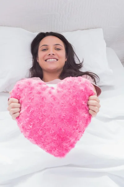 Woman lying in her bed and holding a fluffy heart cushion — Stock Photo, Image