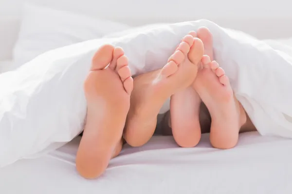 Paar wrijven hun voeten samen onder het dekbed — Stockfoto