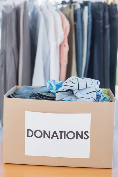 Caixa de doações cheia de roupas na frente do corrimão de roupas — Fotografia de Stock