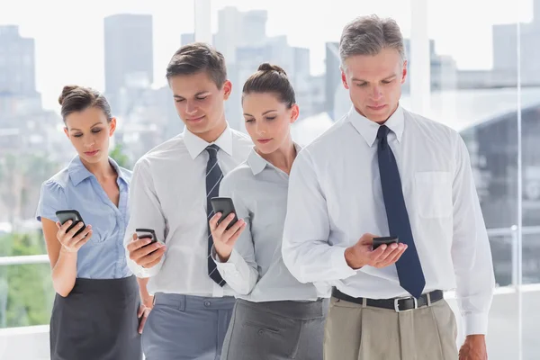 Negócios sérios em pé juntos em linha com seu celular — Fotografia de Stock