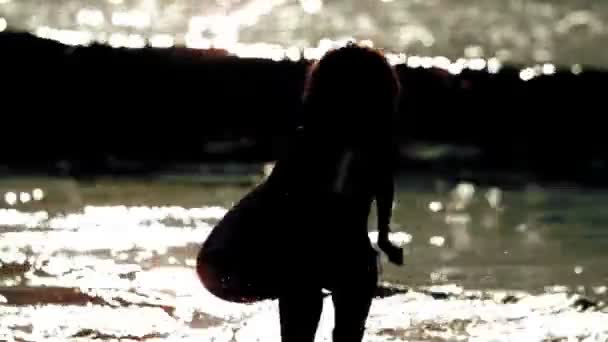 Silhouette di donna che tiene la tavola da surf e corre sulla spiaggia — Video Stock