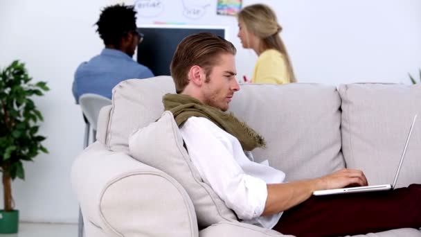 Человек работает на ноутбуке на диване и улыбается — стоковое видео