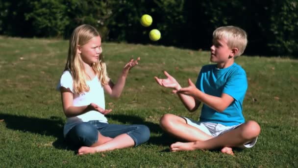 Syskon satt i en park som leker med tennisbollar — Stockvideo