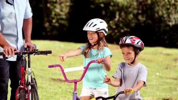 Padres e hijos señalando el camino a seguir mientras van en bicicleta — Vídeos de Stock