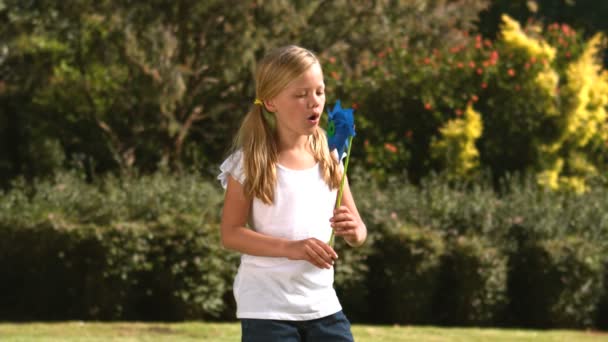 Liten flicka blåser en vindsnurra i hennes trädgård — Stockvideo