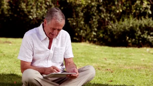 Зрілий чоловік сидів на траві за допомогою планшетного комп'ютера — стокове відео