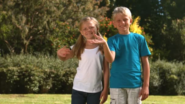 Vrolijke broers en zussen zwaaien samen in hun tuin — Stockvideo