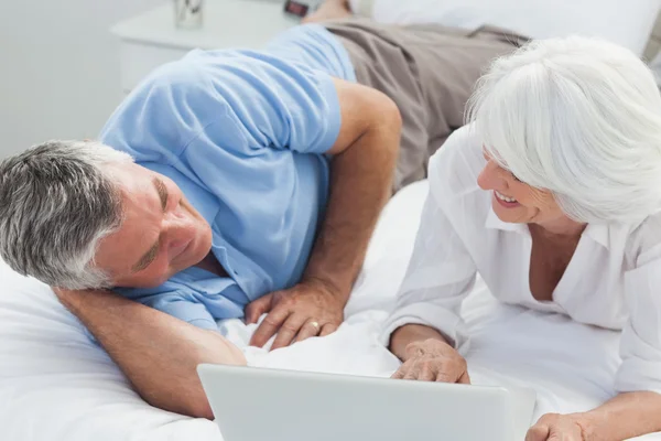 Couple lying in bed and using a laptop — Stock Photo, Image